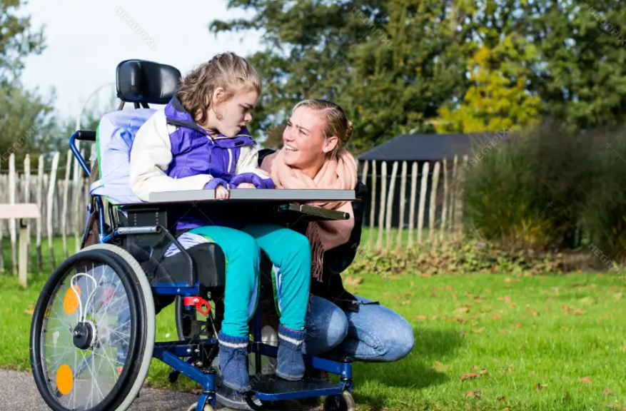 Jente i rullestol på kanskje 10 år, vedsiden av sitter en eldre jente på huk. Bakgrunn er hage og gress. Hun har trolig fått hjelp å søke en BPA